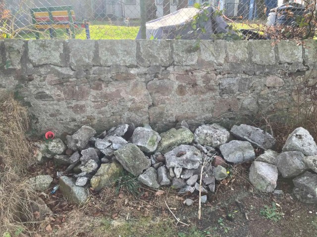 A pile of reclaimed granite and rubble at the base of an old stone wall, ready to be used in the construction of a retaining border wall.