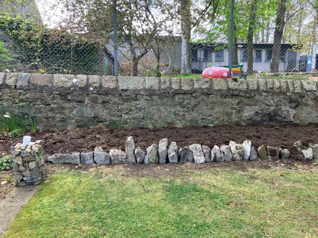 A rustic retaining wall built from upright reclaimed stones along a freshly cleared garden border.